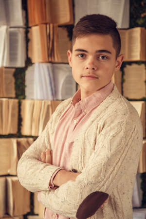 Confident handsome teenager posing in the library and smiling at camera, youth and education concept