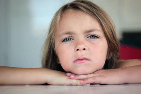 Portrait of cute little girl with head in hands sitting at tableの写真素材