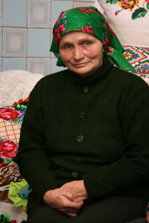 VOLODYMYREC, UKRAINE - 03 November 2008: Senior woman sits on bed with embroidered pillows in rural parlorのeditorial素材