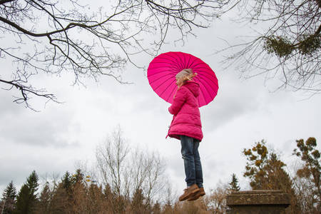 Little girl flying with pink umbrella above autumn park treesの写真素材
