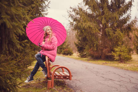 Cute little girl with umbrella sitting on the bench in parkの写真素材