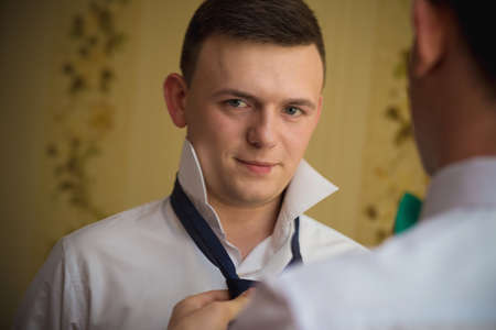 VILHIVKA, UKRAINE - 21 May 2017: Groomsman helps to wear a tie to the groom in room. Shallow depth of field.のeditorial素材