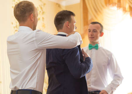 VILHIVKA, UKRAINE - 21 May 2017: Groomsman helps to wear a jacket to the groom in room. Shallow depth of field.のeditorial素材