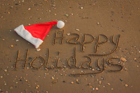The words Happy Holidays written in wet sand with a Santa Hat on a beachの写真素材