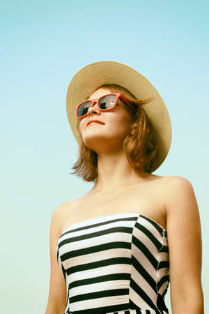 Happy young woman with hat and sunglasses posing over blue skyの写真素材