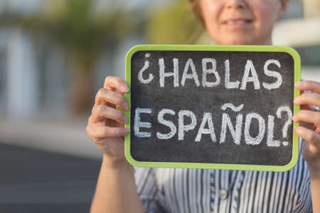 Woman holding a chalkboard with the question habla espanol? Do you speak spanish? Written in spanish is it. Shallow depth of field.の写真素材