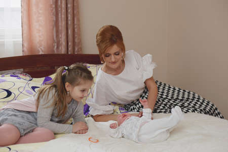 LUTSK, UKRAINE - 26 March 2017: Young mom with daughter and baby dressed playing in the bedのeditorial素材