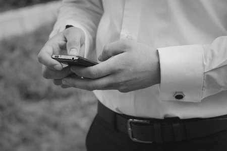 Man in shirt with cufflinks texting on mobile phone at outdoor. Shallow depth of field.の写真素材