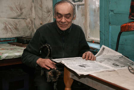 ADAMIVKA, UKRAINE - 26 January 2009: A man sitting at a table reading a newspaper and holding a cat in a country houseのeditorial素材