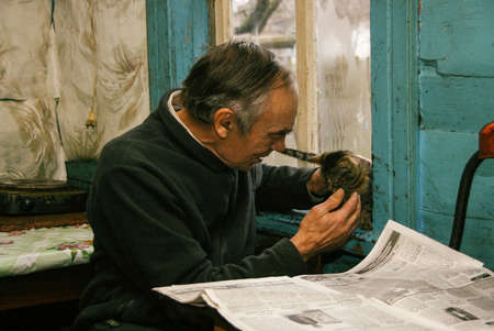 ADAMIVKA, UKRAINE - 26 January 2009: A man playing with kittens and reading a newspaper in a country houseのeditorial素材