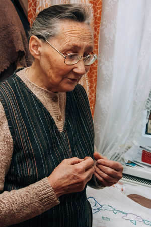 Chortkiv, Ternopil / Ukraine - March 04 2009: Senior woman with eyeglasses stand next window at home