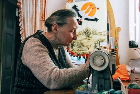 Chortkiv, Ternopil / Ukraine - March 04 2009: Senior woman during sewing on a machine at home