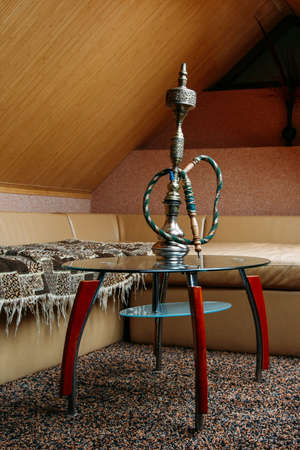 Eastern hookah on a glass table in room with sofa