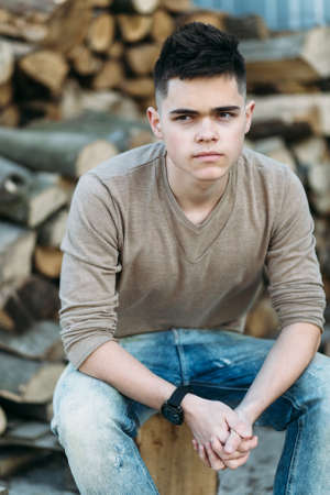 Young man sitting on a log in front of pile of firewoodの写真素材