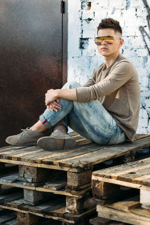 Young handsome man in casual style clothing sitting in front of a wallの写真素材