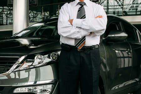 Businessman with arms crossed standing in front of car at showroom