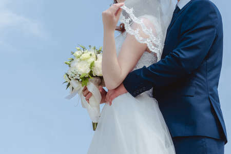 Bride with wedding bouquet and groom posing on sky background