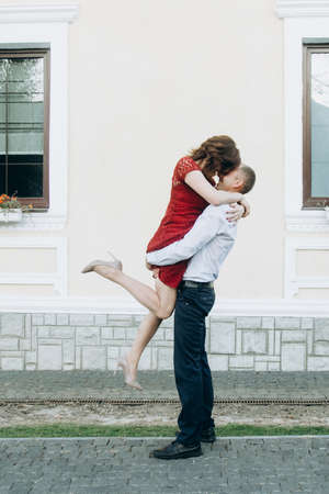 The man is lifting up the woman in his arms on the street at summer