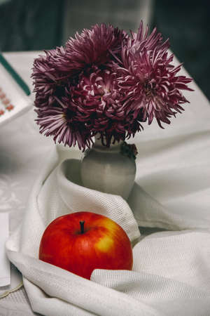Still life with apple and flowers in vase on white fabricの写真素材