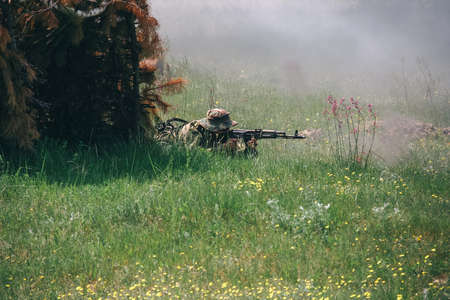 The soldier in camouflage or military with a machine gun shoots out from ambush in the grass....