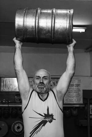 Novograd, Volyn / Ukraine - March 31 2009: Senior man lifting heavy barrel in rural gymのeditorial素材