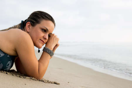 Caucasian woman wearing bikini and jewelry - bracelet - relaxing on beach. Model lying down on sand on vacation travelの写真素材