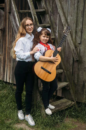 Rokyni, Volyn / Ukraine - May 29 2019: Woman and small girl posing with acoustic guitar next to wooden wall in parkのeditorial素材