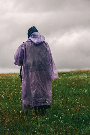 Senior woman in raincoat with stick in the field, enjoying silence and harmony of nature