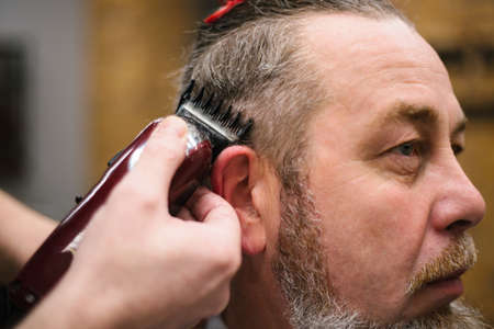 Men's hairstyling and haircutting with hair clipper in a barber shop or hair salon. Shallow depth of field.の写真素材