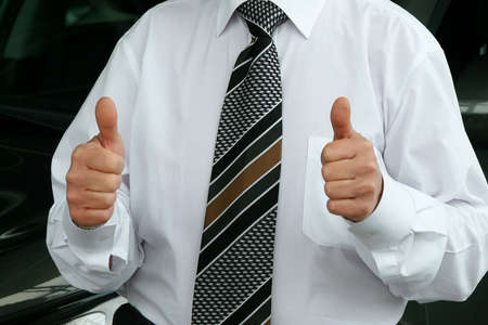 Cropped view of businessman wearing white shirt and tie showing thumbs up next to car