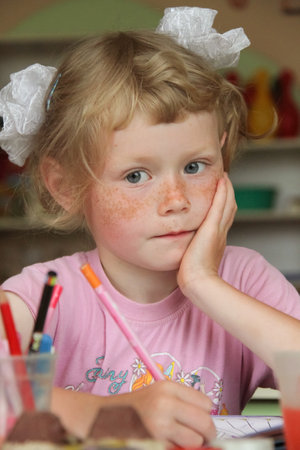 Lutsk, Ukraine - May 14 2013: Small girl with freckles and bows posing with pencil and album for drawing at kindergartenのeditorial素材