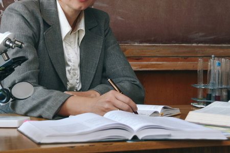 Teacher chemistry woman sitting at the table and writing on notepad chalkboard background. Education concept.の写真素材