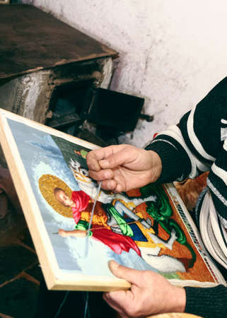 Close up hand of man while embroidery religious icon at rural home with needleの写真素材