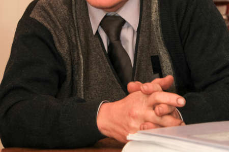 Close-up of man sitting at table with clasped hands. Shallow depth of field.