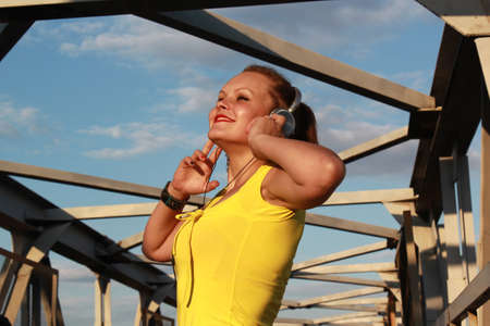 Young woman in headphones listens to music on the pedestrian bridge at city