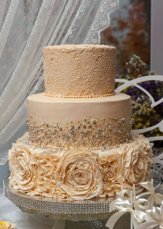 Large Three-tiered wedding or birthday cake decorated with flowers stands on the tableの写真素材