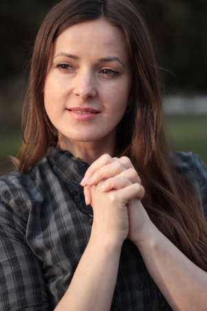 Woman in casual clothing put her hands together, fingers intertwined and praying at outdoors