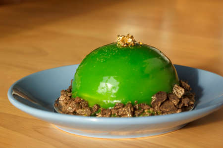 Green mousse cake with mirror glaze on saucer. Dessert for birthday party. Shallow depth of field.の写真素材