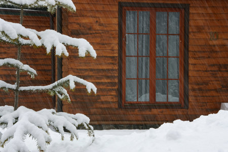 Wall with a window of a wooden house and tree branches covered with snowの写真素材