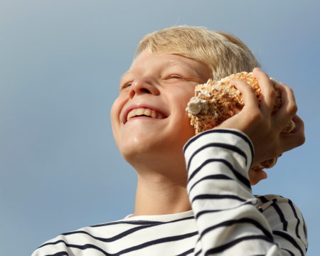 Happy caucasian boy listen to seashell at the sky background