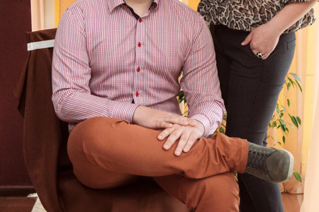 Man sits in the chair. Woman stands near. Cropped view.の写真素材