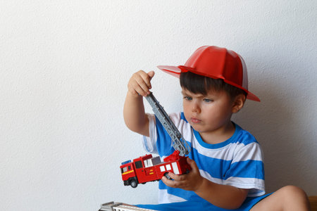 Dark-haired boy in fireman hat plays with toy fire trucks on the floor at home