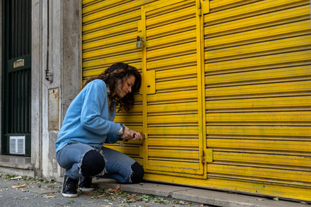 A young Latin American woman opens the lock on the door of her business with difficulty.の写真素材