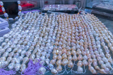 Multicolored baroque pearl strings attached arranged neatly in glass cabinetの写真素材