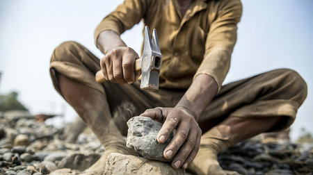 traditional stone carving showing physical effort and craftsmanship in dusty terrainの素材