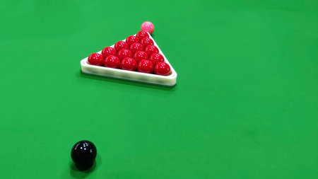 A snooker table with red balls racked and black ball ready for the break