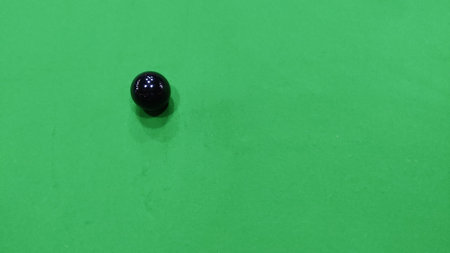 Black ball with white spots on a green surface in a simple composition