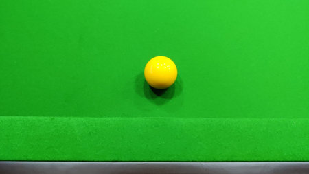 A yellow snooker ball resting on a green snooker table in a close up shot