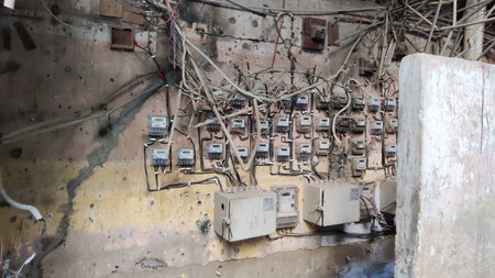 Electric meters on damaged wall with tangled wires showing unsafe power setup, Karachi Pakistan...