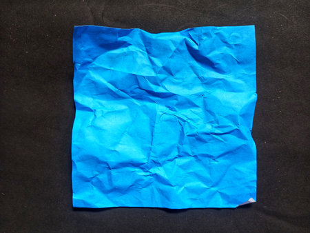 Crumpled blue paper placed on black background, viewed from above. Minimal abstract paper texture...